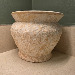 May include: A large, beige ceramic planter with a speckled pattern. The pot has a wide, slightly flared rim and a rounded body, perfect for indoor or outdoor plants. The planter is approximately 12 inches in diameter.