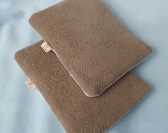 Peut inclure: Deux housses de coussin en polaire marron avec des coutures blanches. Les housses sont empilées l'une sur l'autre. La housse du dessus a une petite étiquette blanche avec un logo.
