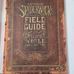 May include: A brown hardcover book with gold lettering, titled "Arthur Spiderwick's Field Guide to the Fantastical World Around You." The cover features decorative borders and a vintage, distressed look.