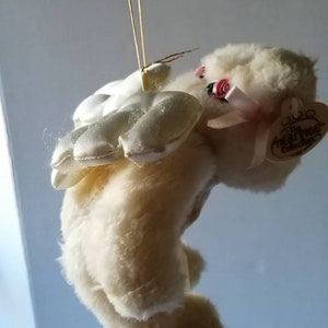May include: White plush angel bear with pink satin wings and a pink bow. The bear has a pink rose on its head and a tag that reads "The Real Rose Collection".