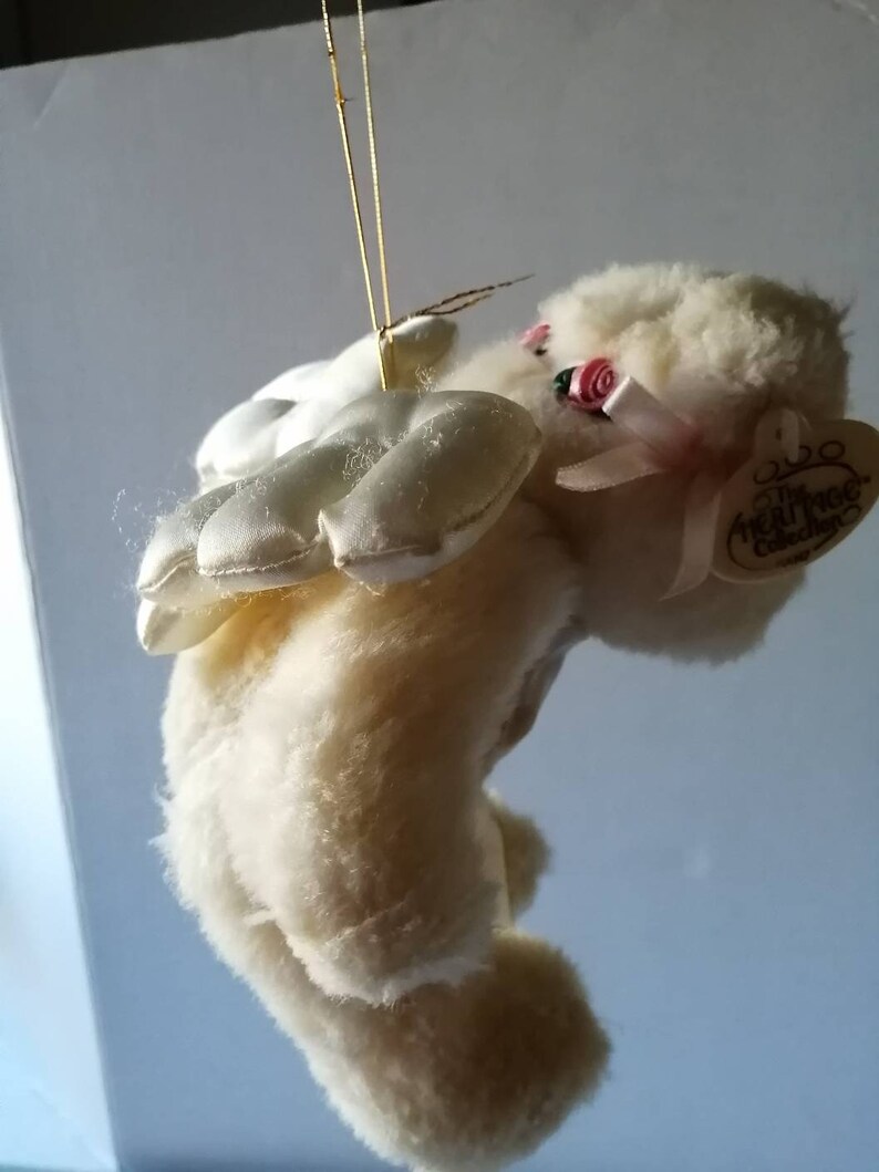 May include: White plush angel bear with pink satin wings and a pink bow. The bear has a pink rose on its head and a tag that reads "The Real Rose Collection".