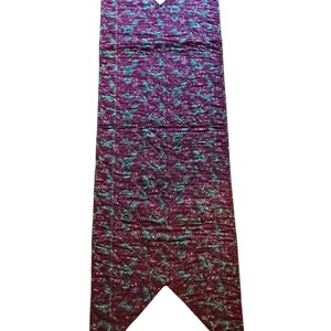 May include: A burgundy table runner with a green floral pattern. The runner is quilted and has a pointed end.