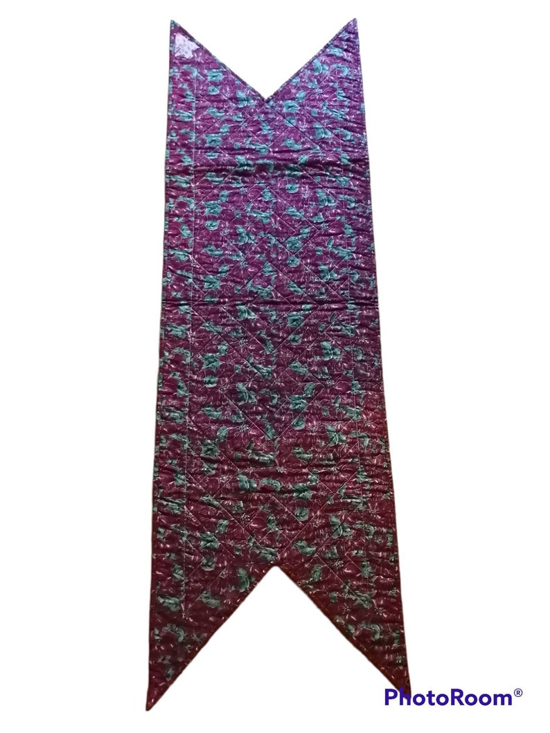 May include: A burgundy table runner with a green floral pattern. The runner is quilted and has a pointed end.