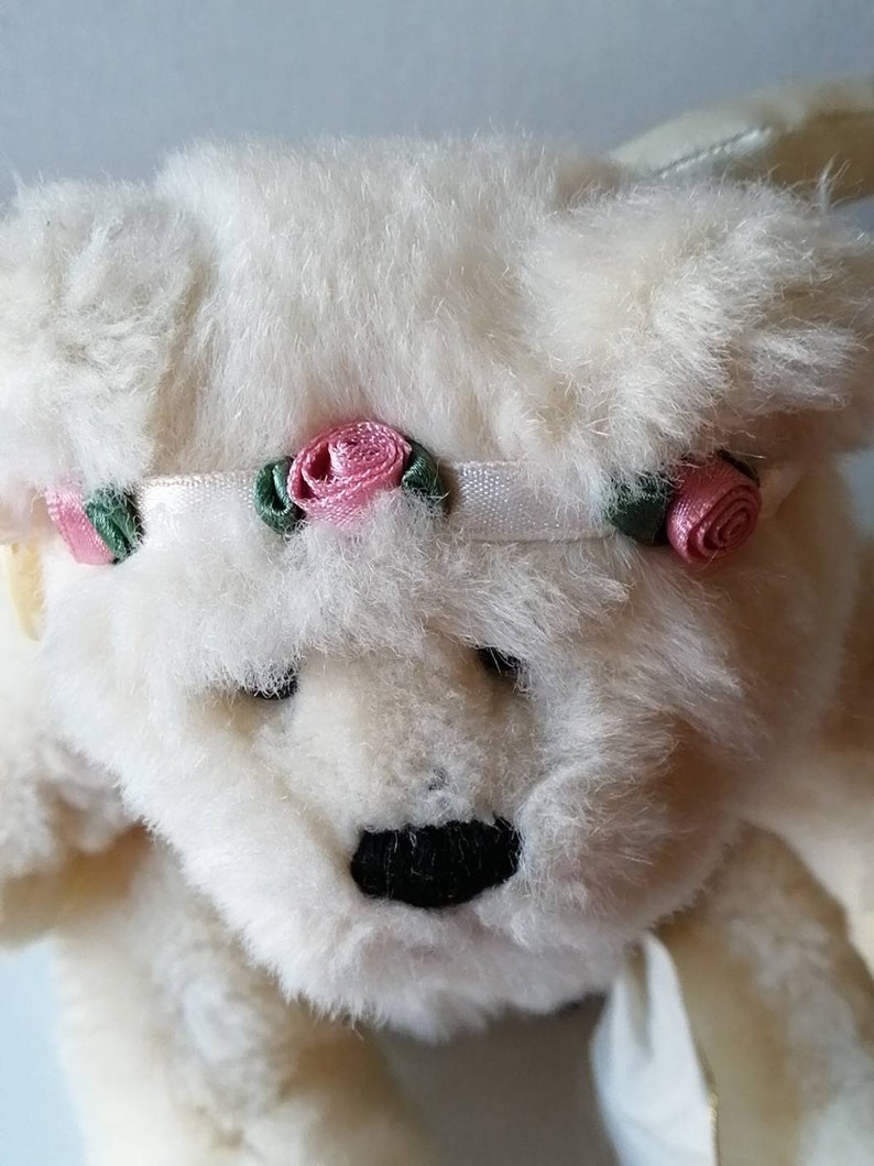 May include: White plush teddy bear with a white headband decorated with pink and green fabric roses.