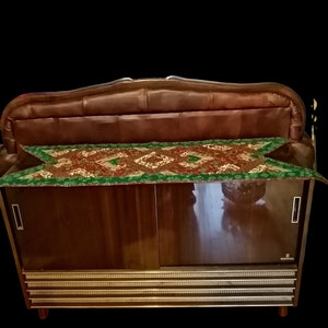 May include: A vintage wooden cabinet with a brown leather top and a gold trim. The cabinet has two doors and a shelf inside. The cabinet is decorated with a green and brown patterned fabric.