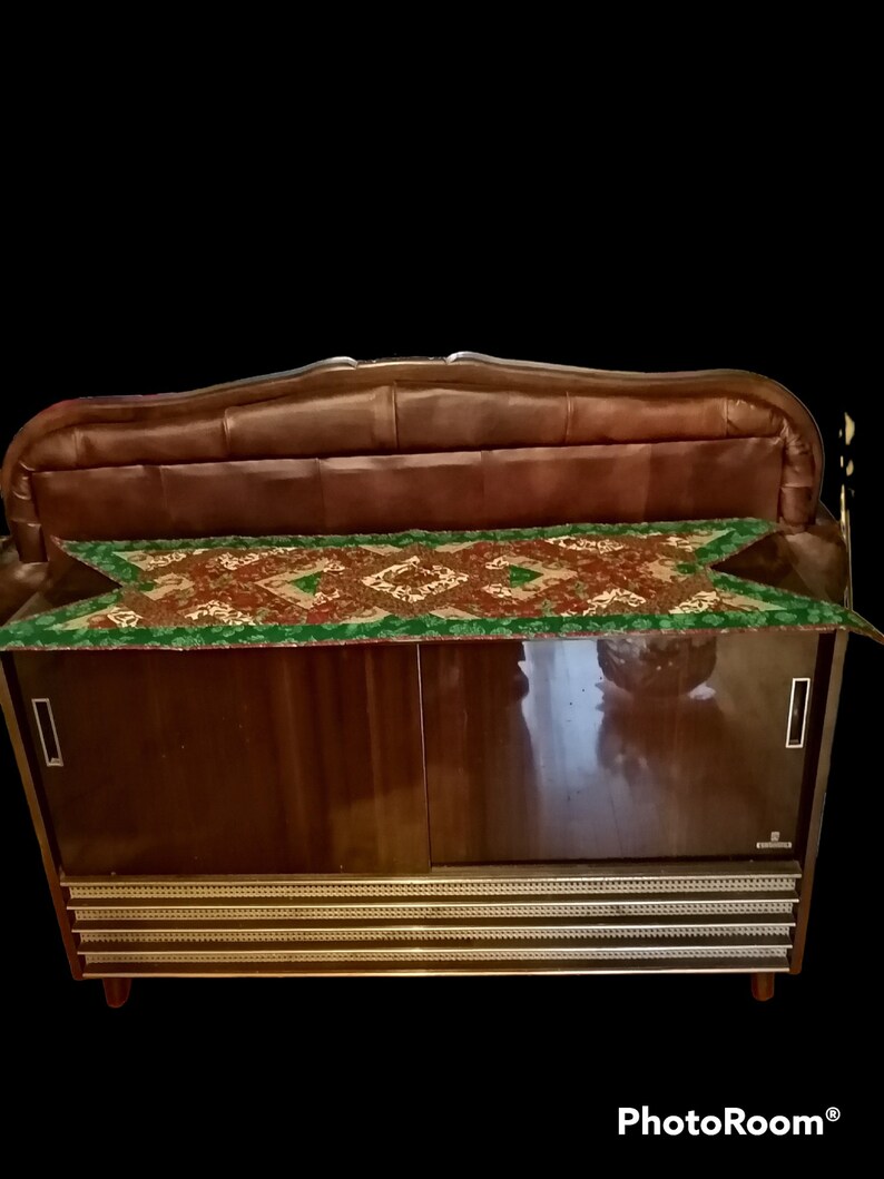 May include: A vintage wooden cabinet with a brown leather top and a gold trim. The cabinet has two doors and a shelf inside. The cabinet is decorated with a green and brown patterned fabric.