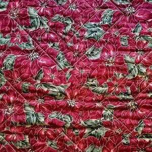 May include: Red quilted fabric with a repeating pattern of poinsettia flowers and green leaves.