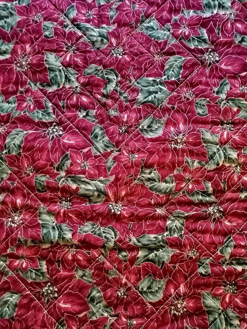 May include: Red quilted fabric with a repeating pattern of poinsettia flowers and green leaves.