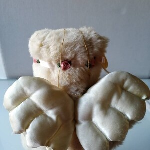 May include: A white plush angel with pink rose accents and satin wings. The angel is a decorative item.