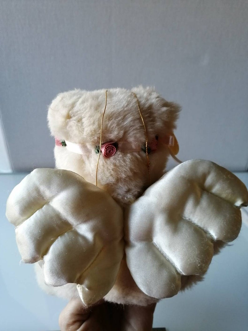 May include: A white plush angel with pink rose accents and satin wings. The angel is a decorative item.