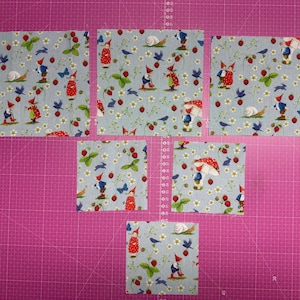 Peut inclure: Sept carrés de tissu bleu clair avec un motif fantaisiste de gnomes, de fraises, d'oiseaux et d'escargots. Les carrés de tissu sont disposés sur un tapis de coupe rose, idéal pour le quilting ou l'artisanat.