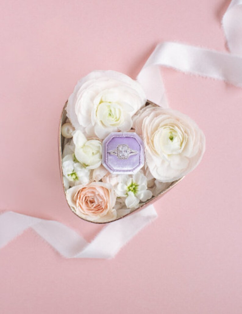 May include: A heart-shaped box filled with white and peach flowers, with a purple ring box containing a diamond ring in the center.
