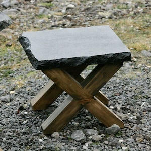 May include: A small black stone table with a rough, uneven edge. The table has a wooden base with an X-shaped design.