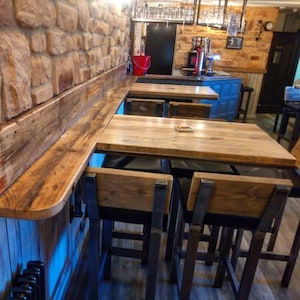 May include: A rustic wooden bar counter with a reclaimed wood top and metal brackets. The counter is topped with a wooden table and four black metal bar stools with wooden seats.
