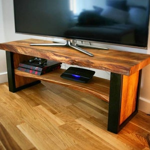 May include: A wooden TV stand with a live edge top and black metal legs. The stand has a shelf for storage and is made of natural wood.