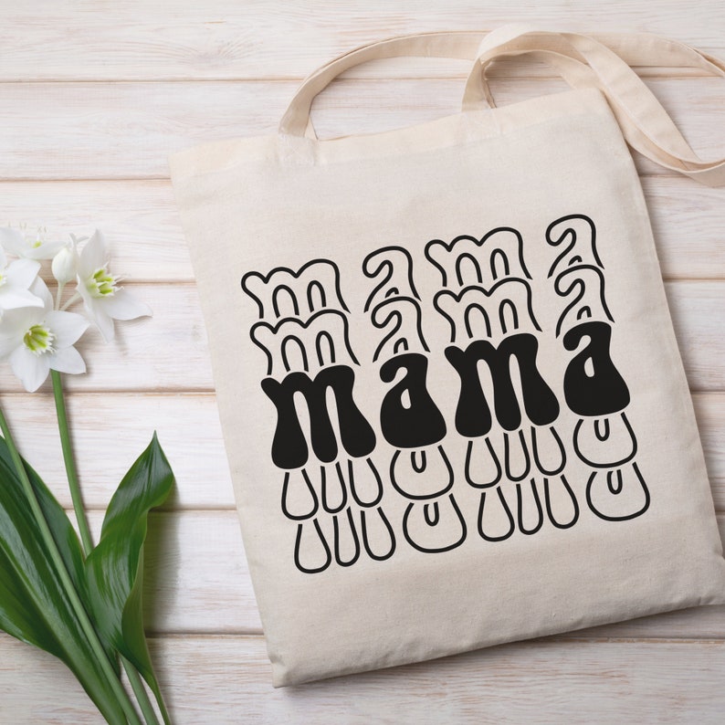 May include: A white canvas tote bag with black text that reads "mama" in a retro, wavy font.