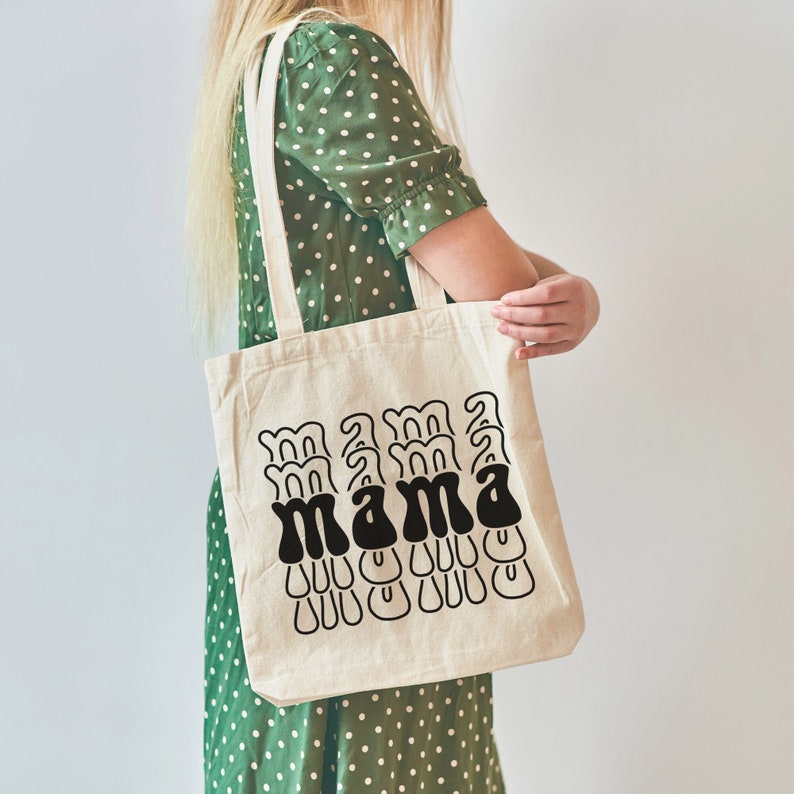 May include: A white canvas tote bag with black text that reads "mama" in a retro font. The text is repeated multiple times in a layered design.