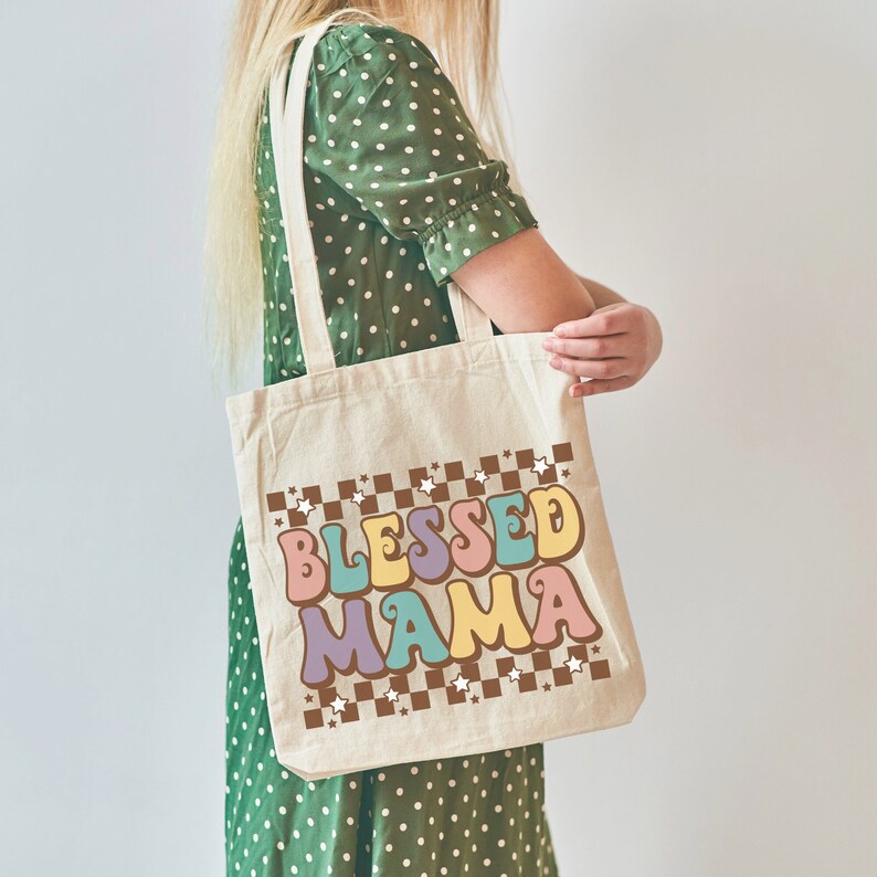 May include: A beige tote bag with brown and white checkered trim and white stars. The bag has the text "Blessed Mama" in colorful retro-style lettering.