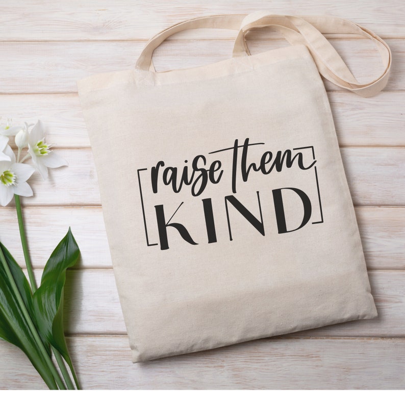 May include: A white canvas tote bag with black text that reads "raise them KIND" in a handwritten font.