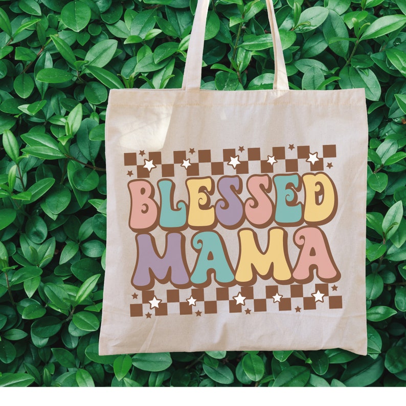 May include: A beige tote bag with a checkered pattern and stars. The text "Blessed Mama" is written in colorful, retro-style letters.