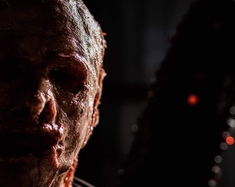 May include: Close-up of a bloody, disfigured face with a dark background.