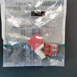 May include: A clear plastic bag containing red and white network modules. The bag has a green stripe and the brand name "PANDUIT" printed on it. The modules are red with white and colored accents.