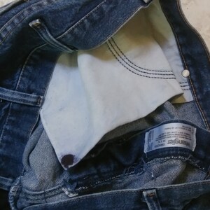 K&ouml;nnte beinhalten: Nahaufnahme einer blauen Jeans mit sichtbarem wei&szlig;em Taschenfutter. Die Jeans hat ein klassisches F&uuml;nf-Taschen-Design mit Knopf- und Rei&szlig;verschluss. Das Wrangler-Markenetikett ist sichtbar.