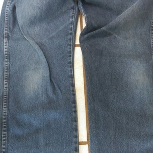 K&ouml;nnte beinhalten: Nahaufnahme einer blauen Jeans. Die Jeans ist gefaltet und zeigt die Vorderseite der Beine. Der Denim hat ein verwaschenes Aussehen mit helleren Bereichen. Die N&auml;hte und Steppn&auml;hte sind sichtbar.