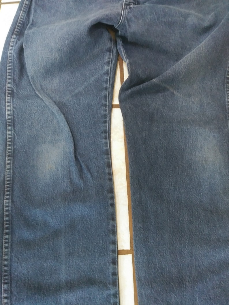 K&ouml;nnte beinhalten: Nahaufnahme einer blauen Jeans. Die Jeans ist gefaltet und zeigt die Vorderseite der Beine. Der Denim hat ein verwaschenes Aussehen mit helleren Bereichen. Die N&auml;hte und Steppn&auml;hte sind sichtbar.