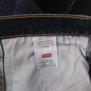May include: A close-up of a Wrangler jeans label showing the size 34 x 32, style number 1096FXVMF, and other product details. The label is white with black text and a red Wrangler logo.