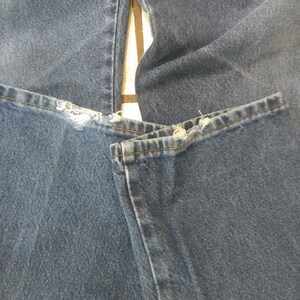 K&ouml;nnte beinhalten: Nahaufnahme einer blauen Jeans mit ausgefransten Details am Saum. Die Jeans ist gefaltet und zeigt die Textur und Farbe des Stoffes. Die N&auml;hte sind entlang der N&auml;hte sichtbar.