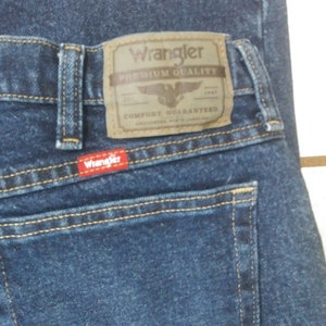 May include: A pair of blue denim jeans with a brown leather Wrangler label that says "Premium Quality" and "Comfort Guaranteed".