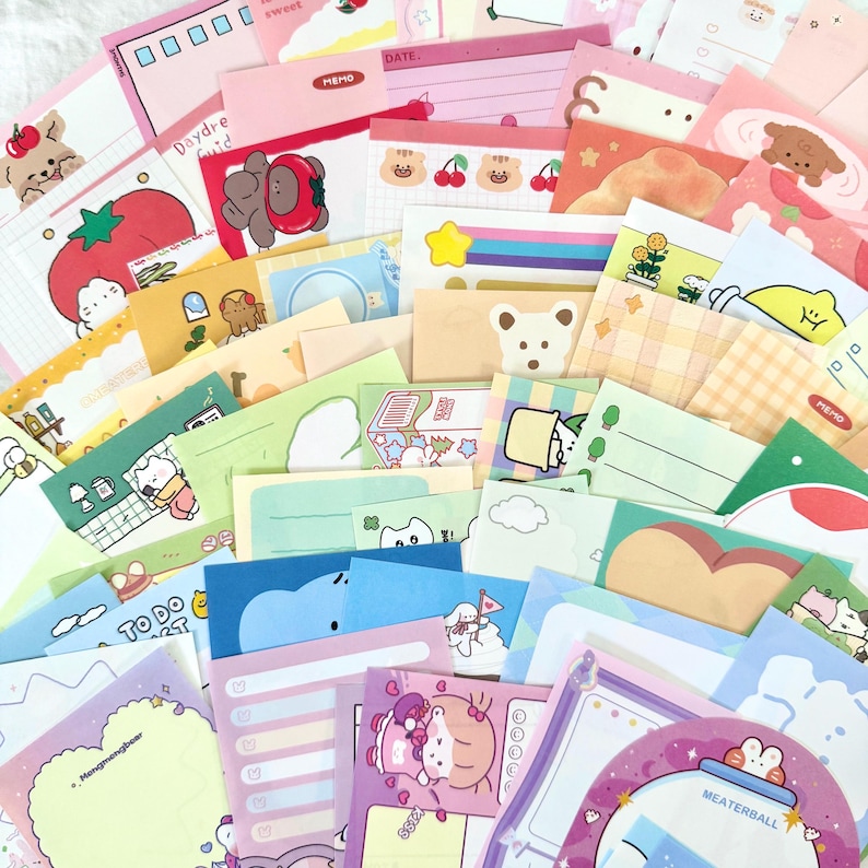 May include: A large collection of colourful memo pads and sticky notes featuring various cartoon characters, animals, food items, and patterns. The stationery set includes diverse shapes, pastel and bright colour palettes, and printed text like Memo.