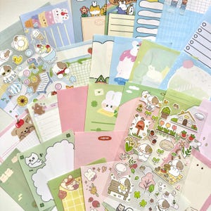 May include: A collection of stationery items including various memo pads, lined note sheets, and clear sticker sheets featuring cartoon animals, food, and floral illustrations in pastel colours. The items include a memo pad with the text MEMO.