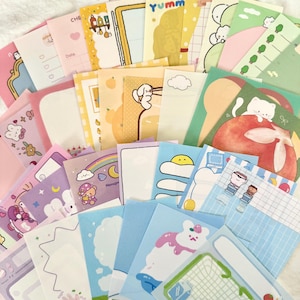 May include: A collection of assorted rectangular memo sheets featuring various pastel-coloured designs, including illustrations of cats, bears, food items, rainbows, and grid patterns, with some sheets displaying the text Yumm and Date.