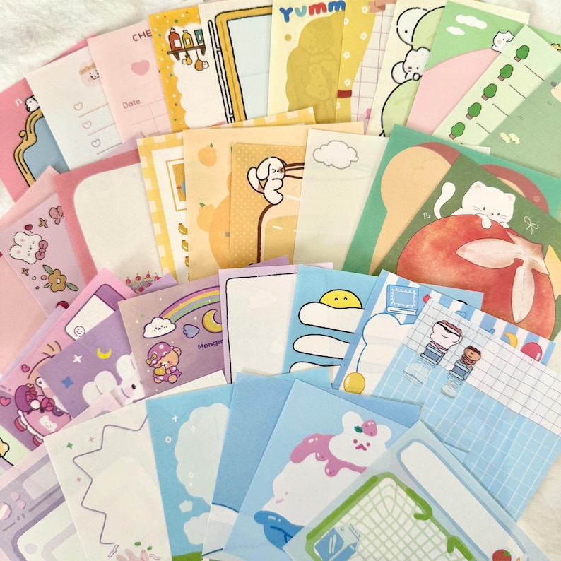 May include: A collection of assorted rectangular memo sheets featuring various pastel-coloured designs, including illustrations of cats, bears, food items, rainbows, and grid patterns, with some sheets displaying the text Yumm and Date.