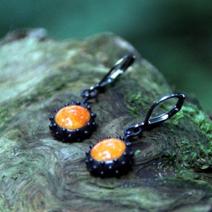 May include: A pair of earrings with orange glass cabochons set in black metal. The earrings have a simple, elegant design and are perfect for everyday wear.