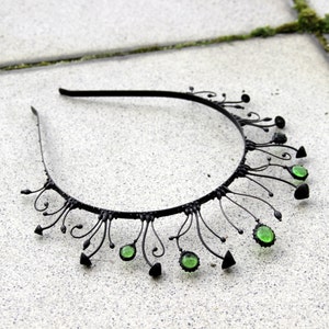 Puede incluir: Diadema de metal negro con detalles de piedras preciosas verdes. La diadema está decorada con delicados diseños de alambre en espiral.