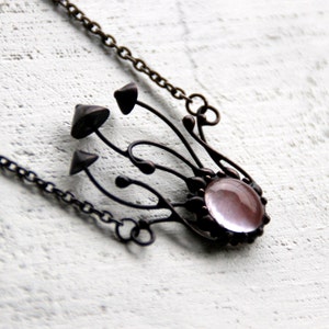 May include: A delicate necklace with a pink glass cabochon surrounded by a detailed metal design resembling a cluster of mushrooms. The chain is made of metal.