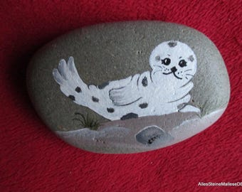 Small seal on the beach, painted stones, stone art, beach landscape on stone.
