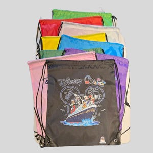 May include: A stack of colourful drawstring bags in green, red, white, yellow, blue, pink, and purple. The front black bag features a graphic of a cruise ship with Disney characters, the text Disney Cruise, and the year 2027 inside a Mickey Mouse icon.