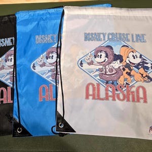 Peut inclure: Trois sacs à cordon Disney Cruise Line Alaska en noir, bleu et blanc. Chaque sac présente un graphisme de Mickey et Minnie Mouse en tenue d'hiver, avec le mot "Alaska" en rouge. Cordons noirs et coins renforcés.