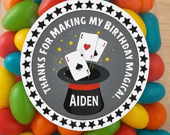 May include: A clear cellophane bag filled with colorful candy. A round sticker with black and white stars and the text "Thanks for making my birthday magical" and the name "Aiden" is attached to the bag. The sticker also features a black and white illustration of a magician's hat with playing cards.