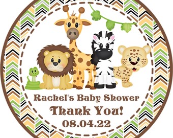 May include: Round, brown and white chevron patterned sticker with a green, brown, and white border. The sticker features a giraffe, lion, zebra, leopard, and snake. The text on the sticker reads "Rachel's Baby Shower Thank You! 08.04.22".