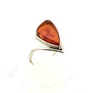 Könnte beinhalten: Ein Silberring mit einem großen, tropfenförmigen Bernstein. Der Bernstein hat eine warme, durchscheinende orange-braune Farbe. Der Ring hat ein silbernes Band und eine Fassung mit einem strukturierten Design um den Bernstein.