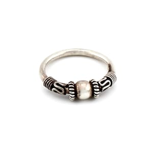 Könnte beinhalten: Ein silberner Ring mit einer zentralen Perle und dekorativen Details. Der Ring hat ein abgerundetes Band mit strukturierten Akzenten auf beiden Seiten der Perle. Das Design hat eine Vintage- oder Antik-Ästhetik.
