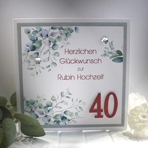 Könnte beinhalten: Quadratische Grußkarte mit weißem Hintergrund, Text "Herzlichen Glückwunsch zur Rubin Hochzeit" und Zahl "40" in rotem Glitzer. Die Karte ist mit Aquarell-Eukalyptusblättern und silbernen Verzierungen verziert.