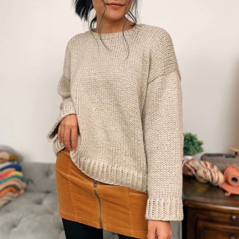 May include: A beige knitted sweater with a relaxed fit and long sleeves. The sweater is made of a soft, chunky yarn and has a slightly oversized look.