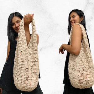 May include: A large, off-white crocheted tote bag with a speckled pattern of brown and red. The bag is worn over the shoulder of a person wearing a black tank top.