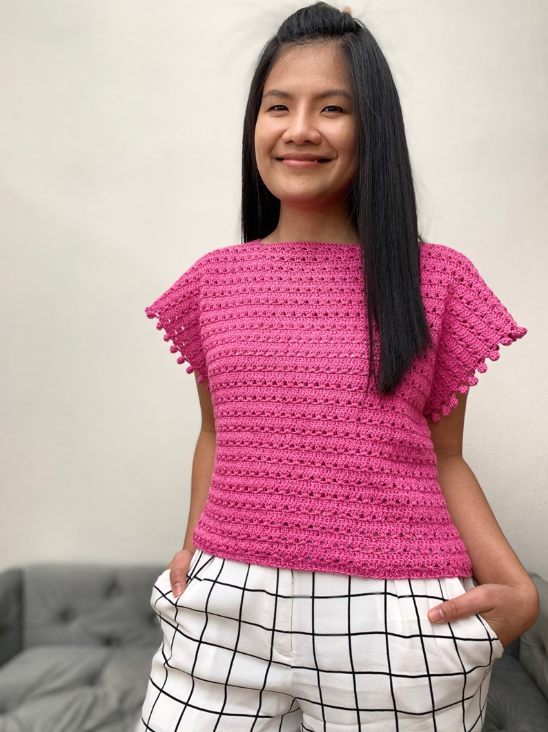 May include: A pink crocheted top with short sleeves and a scalloped edge. The top has a loose fit and is made with a delicate stitch pattern.